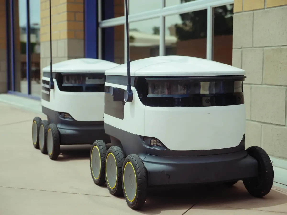 Two autonomous delivery robots positioned outside a modern building, showcasing innovation in robotics and mobility.