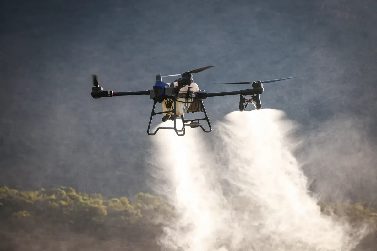 ドローンが緑の田畑上でスプレーやらを散らかしている。現代農業技術と作物管理を示している。